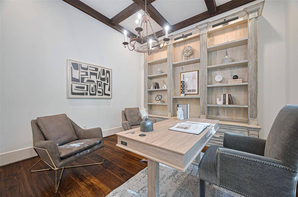Home office, study, or library features a large window with garden views, built-in shelving, and a cozy seating area. It has a chandelier, rich wooden floors, and neutral tones, offering a warm and inviting workspace.