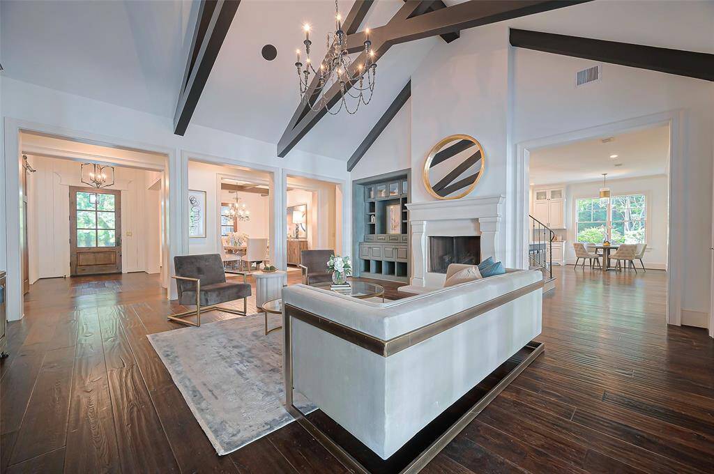 This inviting living room features high ceilings with exposed beams, a grand fireplace, and elegant wood flooring.