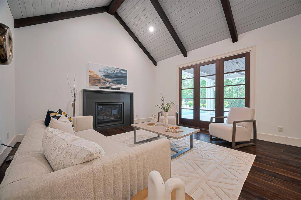 The Den that is open to the kitchen features a vaulted ceiling with exposed beams, a cozy fireplace, and large glass doors providing natural light, creating a warm and inviting atmosphere.
