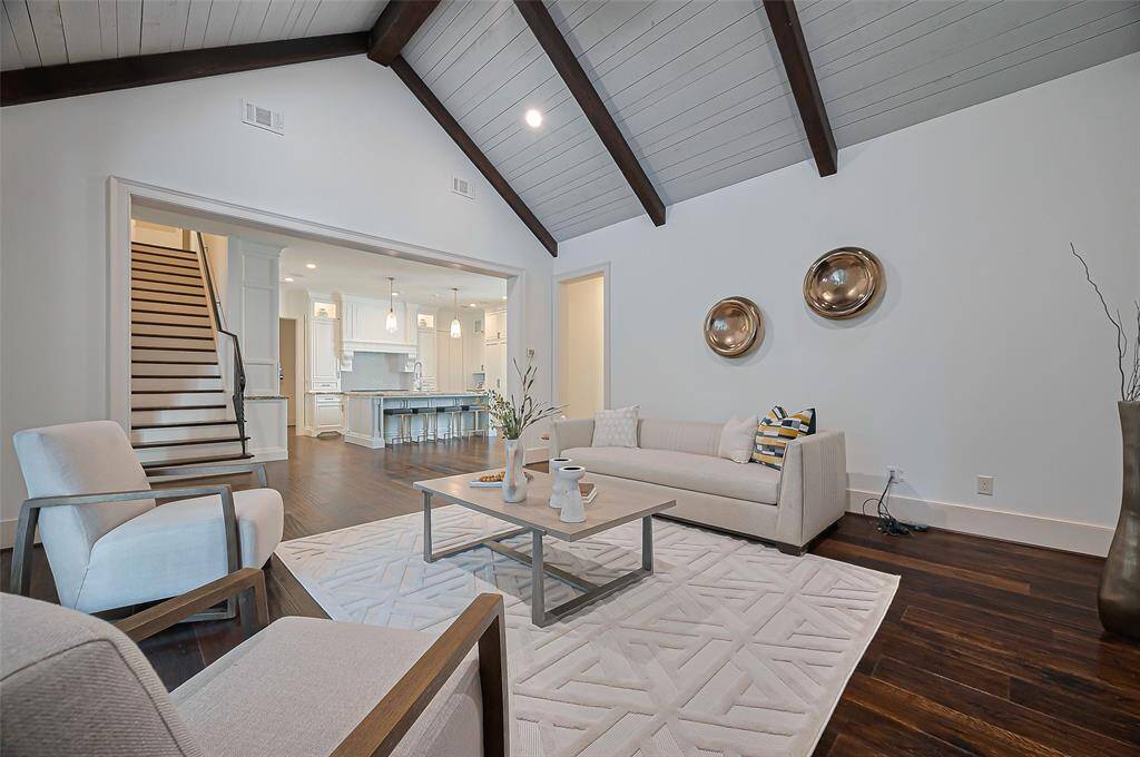 Vaulted ceiling with exposed beams, elegant chandelier, and a cozy fireplace. It seamlessly connects to a dining space and kitchen, all with hardwood floors and ample natural light. The Den opens to a bright, spacious kitchen with a large island, perfect for entertaining or keeping an eye on the family.