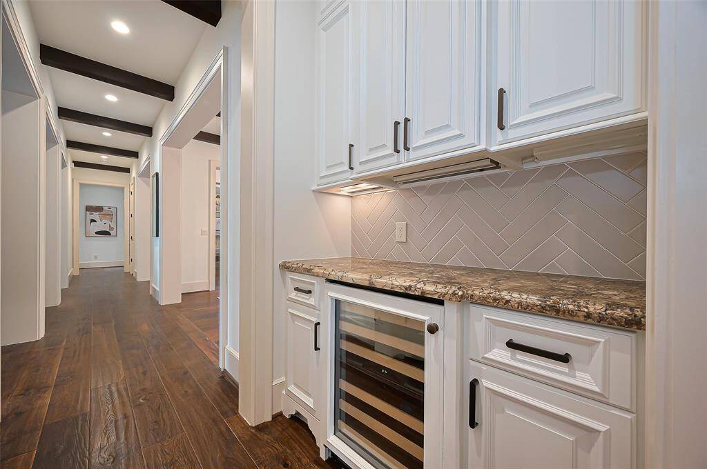 Stylish built-in bar area featuring custom cabinetry, a wine cooler, and a herringbone tile backsplash.