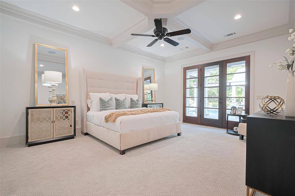 Stunning Primary Suite bright and spacious bedroom. Tray ceilings, a ceiling fan, and large French doors leading to an outdoor pool and tranquil views, creating a serene and luxurious atmosphere.