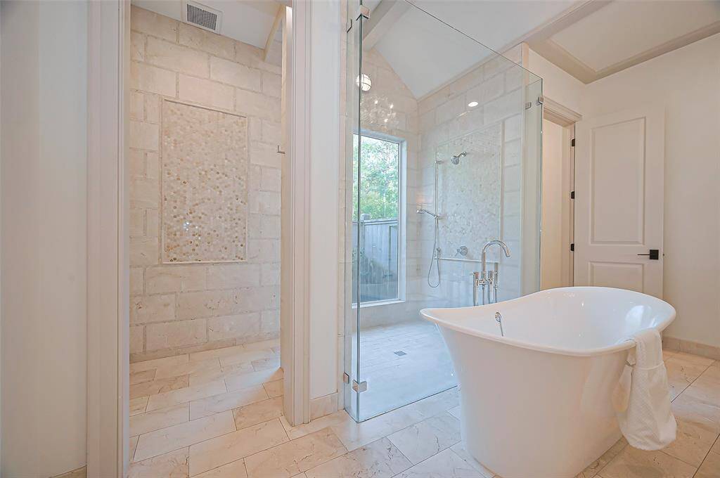 Tastefully designed spacious glass-enclosed shower, a freestanding bathtub, and elegant stone tile flooring. Large windows provide tons of natural light.