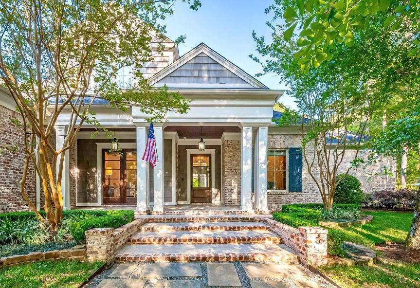 Front porch with classic brick and wood details, complemented by a hanging lantern. The American flag adds a welcoming touch, while large windows provide a glimpse into the cozy interior.