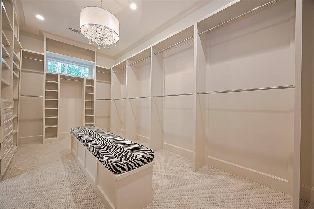 Primary walk-in closet features ample shelving and hanging space, a stylish zebra-print bench, and elegant lighting with a chandelier, offering both functionality and luxury.