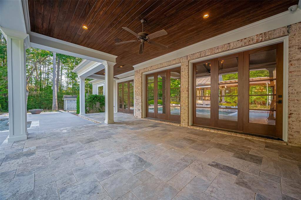 Have morning coffee on this overed outdoor patio with elegant stone flooring and wooden ceiling. Large glass doors provide a view of a pool area, surrounded by trees for a serene, total private setting. Ideal for entertaining or relaxing.