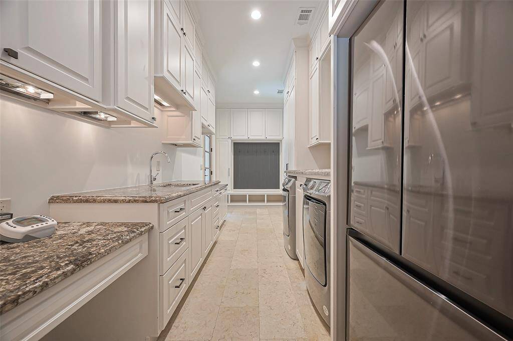 Now this is a wonderful laundry/mud room, tons of cabinetry for storage, sink, granite countertops. The room has a neutral tile floor and recessed lighting, creating a clean functional space. Note: Refrigerator stays, Washer/Dryer has been removed.