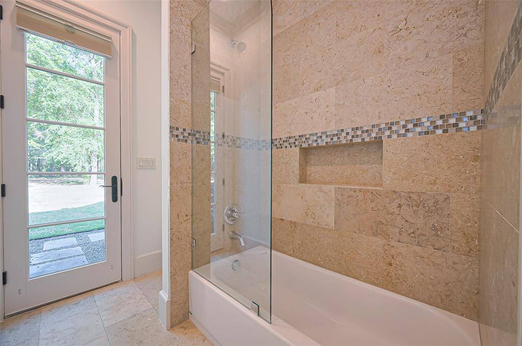 Downstairs Guest Bedroom Bath, glass-enclosed bathtub and elegant tilework. A large, windowed door provides natural light and access to an outdoor area, creating a bright and inviting space your guests will love.