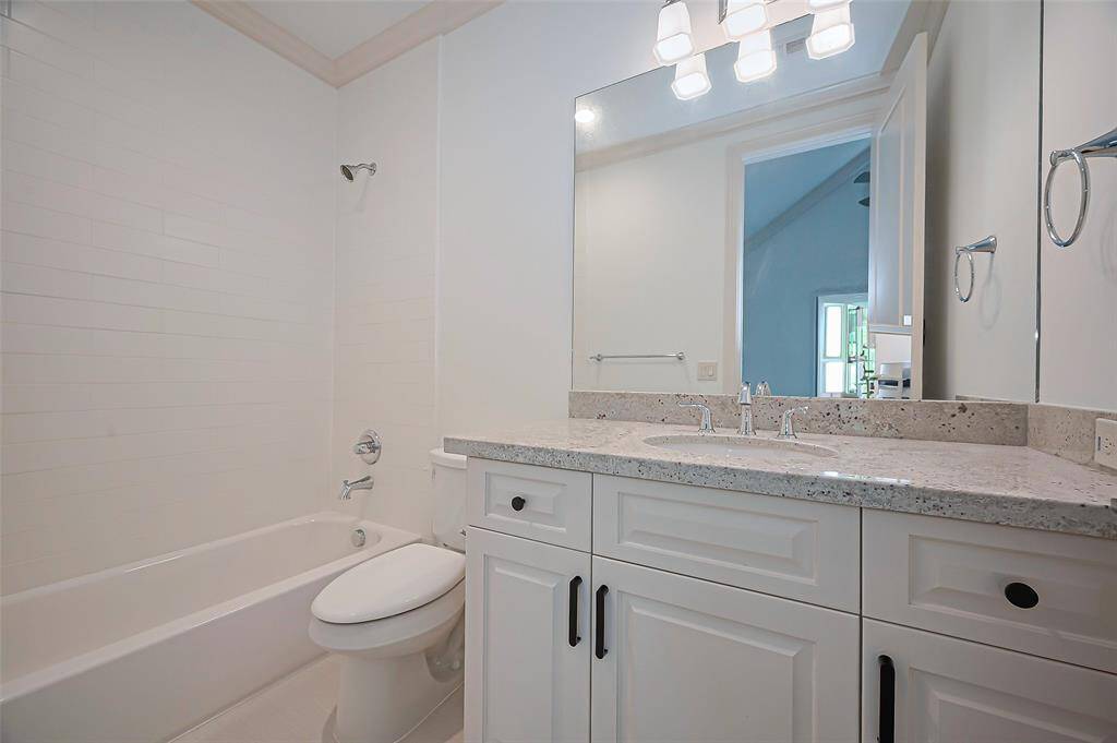 3rd Bedroom ensuite bath with granite countertop and soft close cabinetry. It includes a bathtub with a shower, a large mirror, and bright lighting, providing a fresh and functional space.