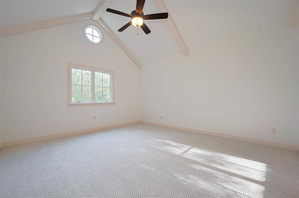 4th Bedroom bright, airy room with vaulted ceiling and exposed beams, featuring a ceiling fan and a round window above a larger window. The NEW neutral carpet the children will enjoy under their feet.