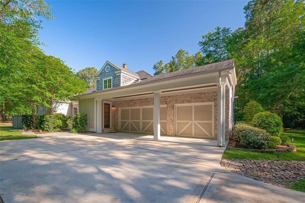 Charming home with a spacious driveway leading to a 3-car garage. Surrounded by lush greenery, it features a brick and siding exterior with a quaint dormer window, offering both elegance and privacy.