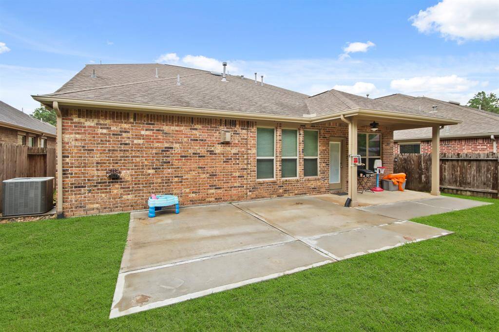 Spacious backyard featuring an extended concrete patio, perfect for outdoor seating, decor, or a barbecue setup. A covered porch right outside the back door provides shade and protection, creating an ideal space for relaxation and entertaining.
