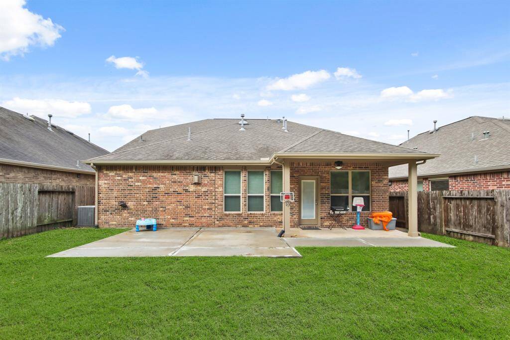 Spacious backyard featuring an extended concrete patio, perfect for outdoor seating, decor, or a barbecue setup. A covered porch right outside the back door provides shade and protection, creating an ideal space for relaxation and entertaining.