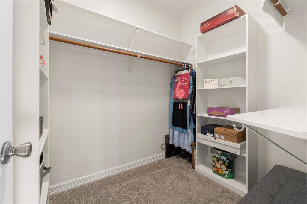 Spacious walk-in closet with built-in shelves and ample hanging space, featuring neutral carpeting and a clean, organized layout. Perfect for storage and organization.