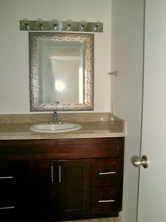 This bathroom features a modern vanity with a dark wood finish, granite countertop, and an elegant framed mirror. There's ample storage with multiple drawers and a sleek light fixture above.