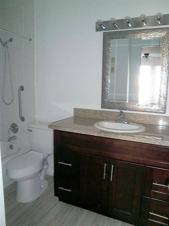 This bathroom features a modern vanity with granite countertop, a large mirror with stylish lighting, a bathtub with shower, and a sleek tile floor.
