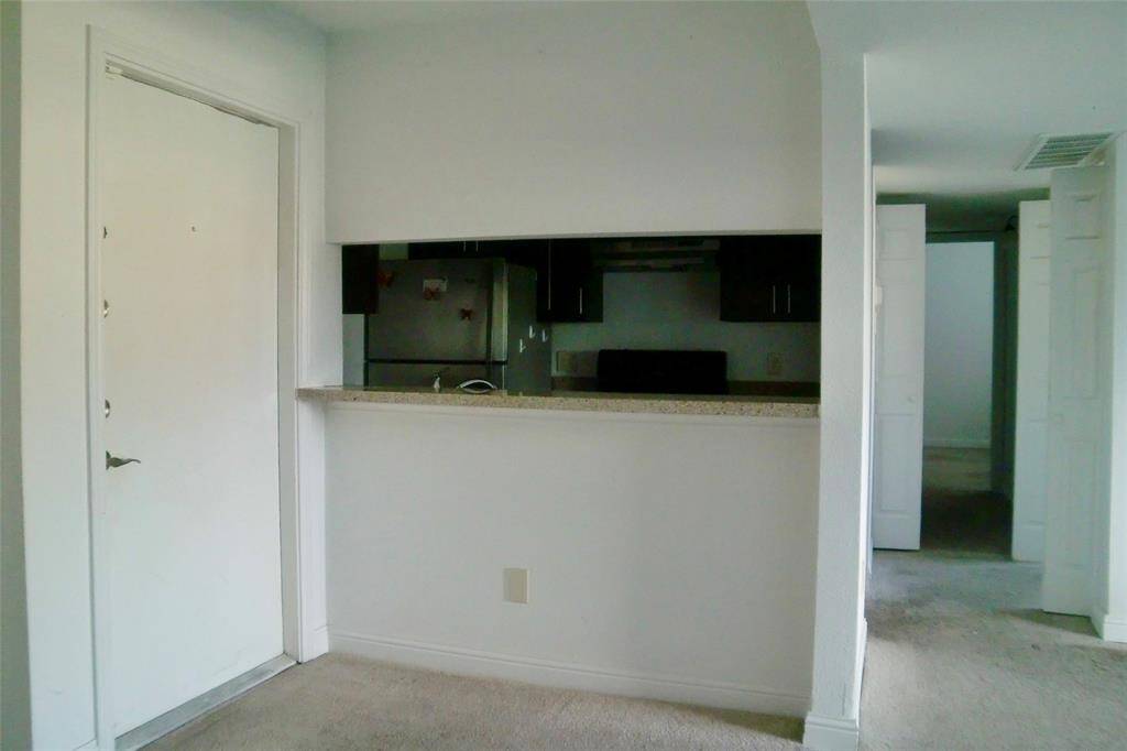 This photo shows a compact, open-concept kitchen area. with a view into an dinning room. The kitchen includes dark cabinetry and a stainless steel refrigerator.