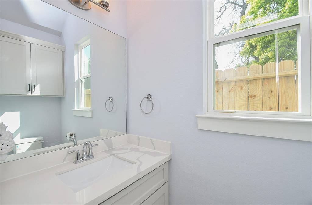 The main level half-bath features beautiful quartz countertops, a stylish mirror, and ample storage space, making it the perfect space to welcome guests and family.