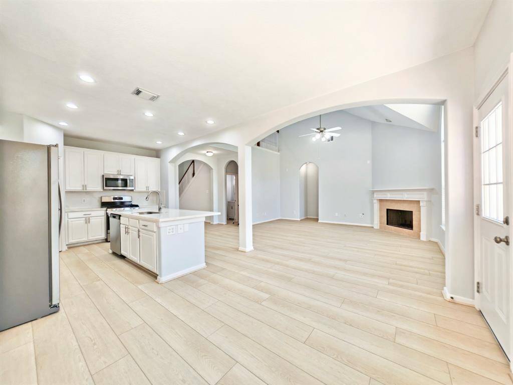 This modern kitchen features white cabinetry, stainless steel appliances, and a spacious marble-look island with a built-in sink. It has an open layout with recessed lighting and arches leading to adjacent spaces.