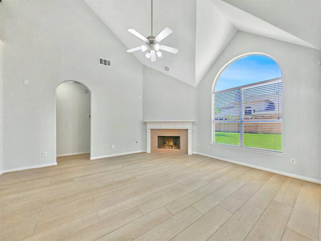 This spacious living room features high vaulted ceilings, a cozy fireplace, and a large arched window that lets in plenty of natural light, offering a bright and inviting atmosphere.