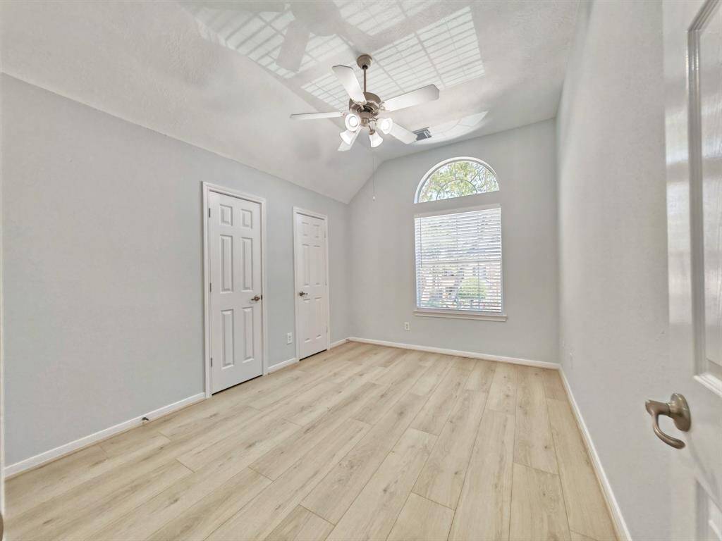 Upstairs 2nd Bedroom with vaulted ceiling and ceiling fan; large arched window; two doors provide access to closets, enhancing storage options.