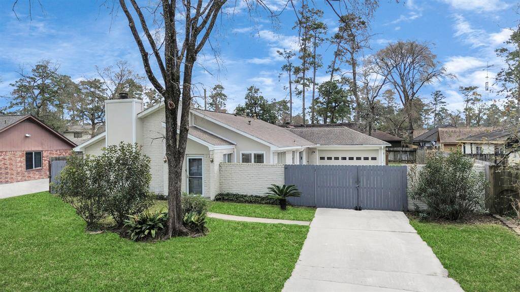 Charming single-story home with a modern exterior, featuring a white facade and a gray fence. It includes a spacious driveway, attached garage, and lush green lawn with mature trees, offering privacy and a welcoming atmosphere.