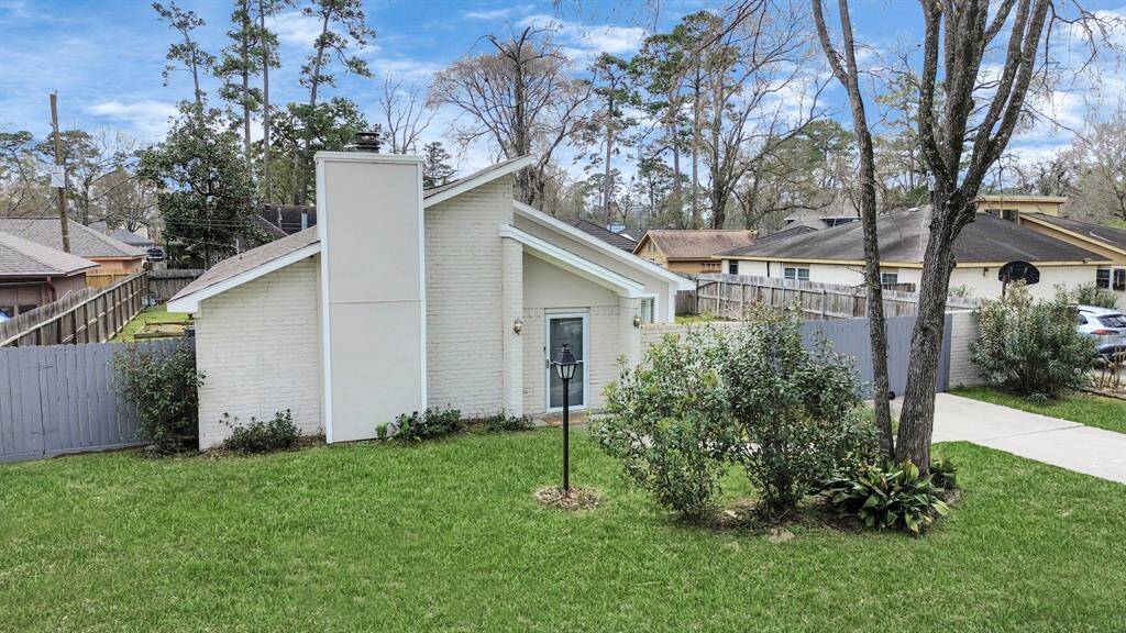 Charming white brick home with a modern sloped roof, set in a spacious, well-maintained yard with mature trees. The property features a paved driveway and a fenced backyard, ideal for privacy and outdoor activities.