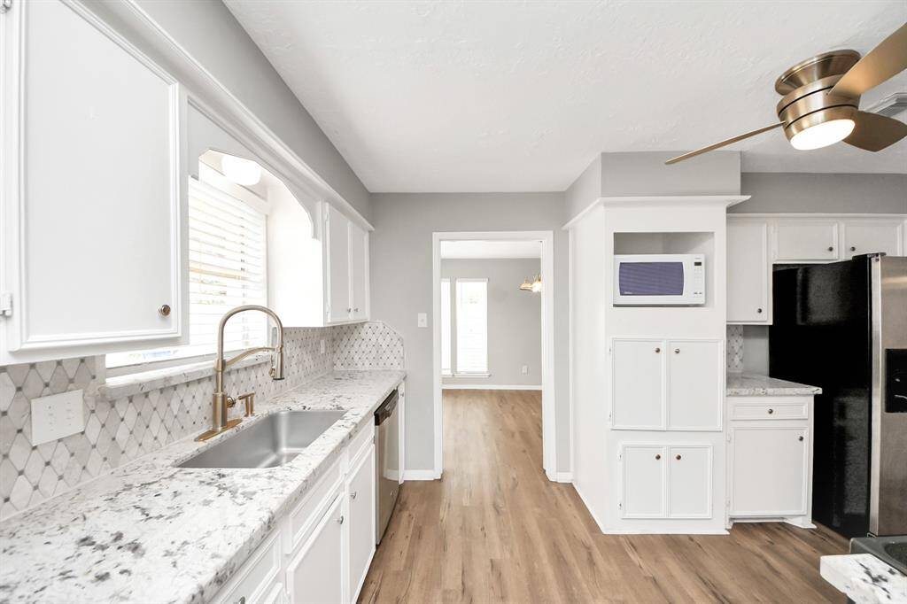 Bright and spacious kitchen with modern white cabinetry, granite countertops, and stainless steel appliances. Features a stylish backsplash, large sink, and wood-look flooring, leading into a well-lit dining area.