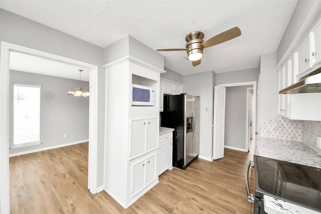 This photo showcases a bright, modern kitchen with stainless steel appliances, white cabinetry, and light wood flooring. A ceiling fan adds comfort, and the adjacent dining area features a stylish light fixture, enhancing the open and inviting space.