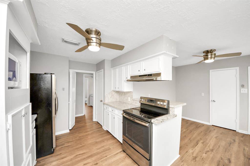 Bright and modern kitchen featuring stainless steel appliances, white cabinetry, and wood flooring. Ceiling fans provide comfort, and the open layout offers ample space for movement.