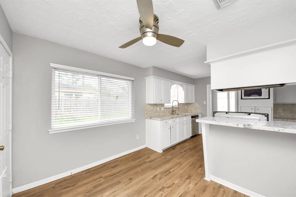 Bright kitchen with modern finishes, featuring white cabinets, a marble countertop, and a wooden floor. A large window provides natural light, and a ceiling fan adds comfort.