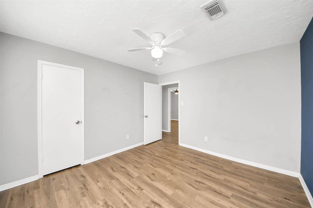 This room features a neutral color scheme with light gray walls and a blue accent wall. It has wood-look flooring and a ceiling fan for comfort. The space includes two doors, offering access to other areas of the home. Bright and functional, it's ideal for a bedroom or office.