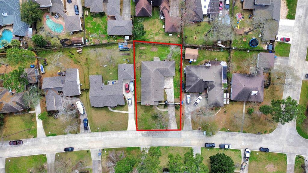 This aerial photo highlights a suburban home marked by a red outline, featuring a spacious backyard and a driveway. It’s situated in a neighborhood with nearby houses, some with pools, on a quiet street.