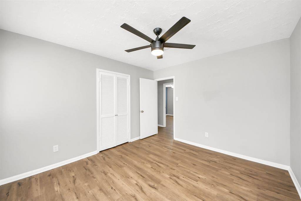 This bright bedroom features modern laminate flooring, a neutral gray color palette, a ceiling fan, and a closet with white louvered doors, offering a clean and inviting space.
