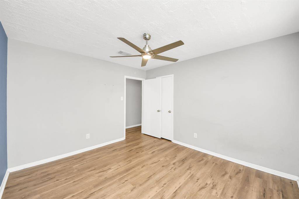 This room features light wood flooring, neutral gray walls, and a modern ceiling fan, creating a bright and airy space. The room includes a closet with white doors, providing ample storage.