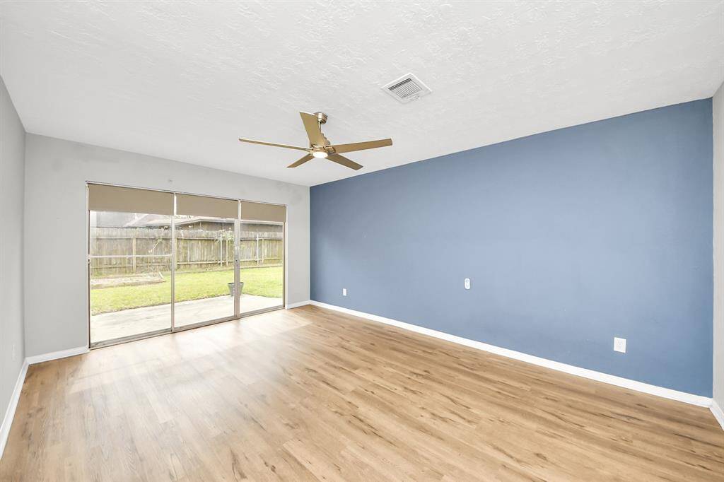 This spacious room features wood flooring, a large blue accent wall, and a ceiling fan. It includes sliding glass doors leading to a backyard with ample natural light.