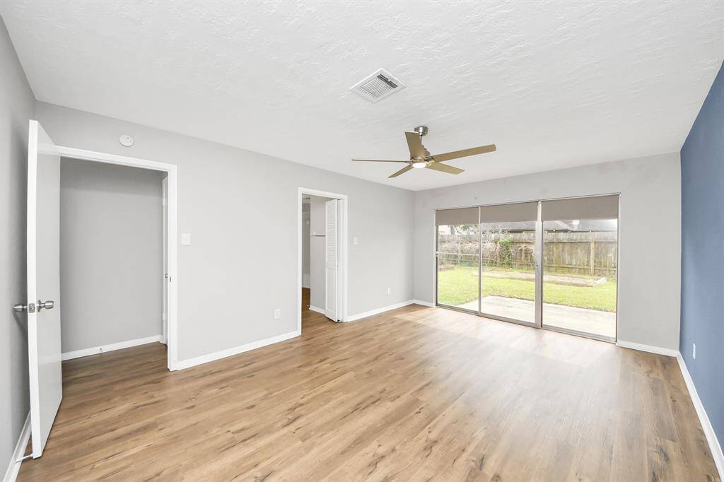 This bright room features laminate wood flooring, a modern ceiling fan, and large sliding doors that open to a backyard, offering plenty of natural light.