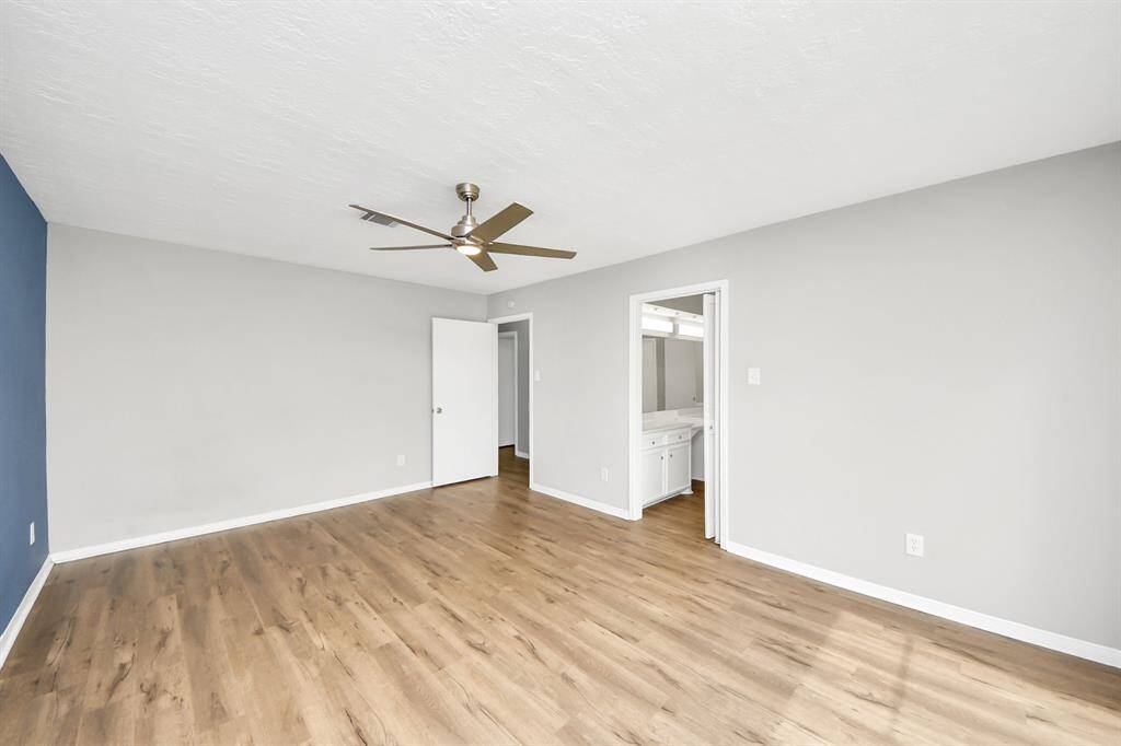 This room features a modern ceiling fan, wood flooring, and neutral walls with a blue accent. It includes an en-suite bathroom and ample natural light, creating a bright and inviting space.