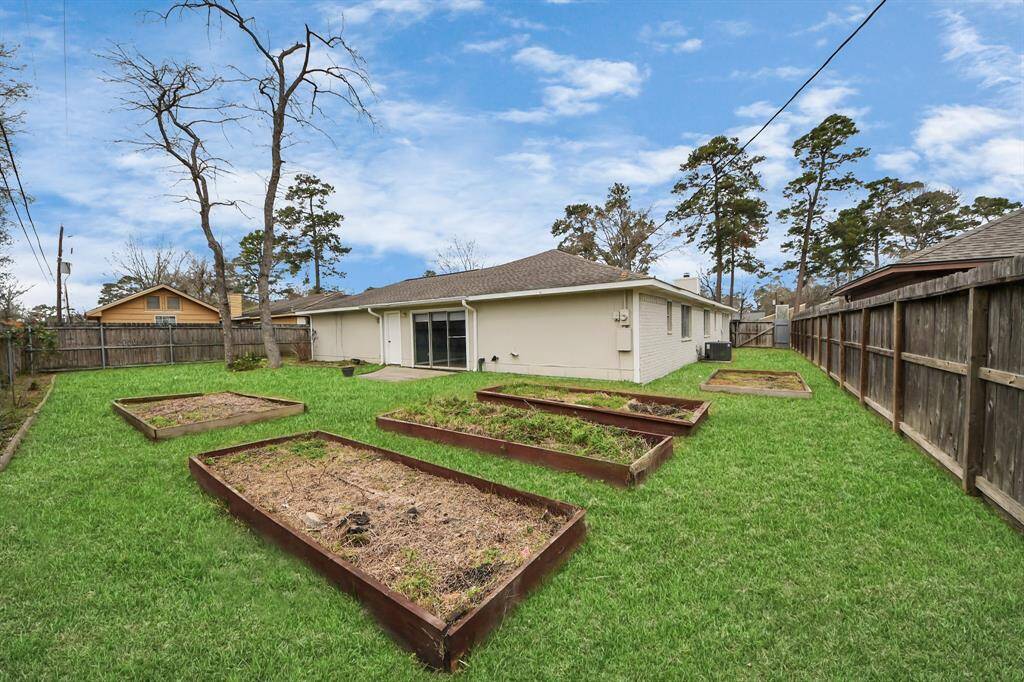 The photo shows a spacious backyard with a well-maintained lawn and multiple raised garden beds. It is fenced for privacy, and the house features sliding glass doors leading to the outdoor space, ideal for gardening or relaxing.