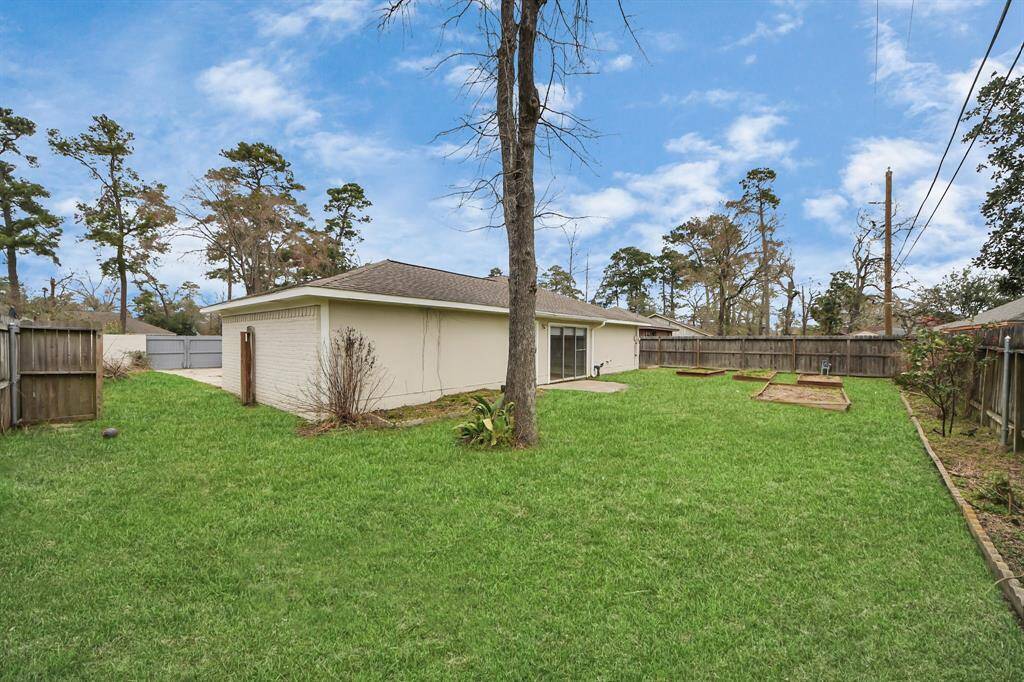 Spacious backyard with lush grass, a mature tree, and garden beds. A white house with a sliding glass door leads to the outdoor area, ideal for relaxation and entertaining.