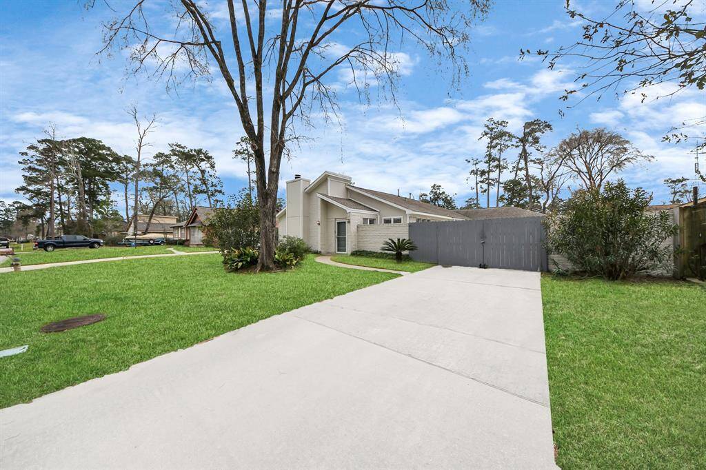 This photo shows a modern, single-story home with a clean, white exterior. It features a spacious driveway leading to a gated area, surrounded by a well-maintained lawn and mature trees, offering a serene suburban setting.