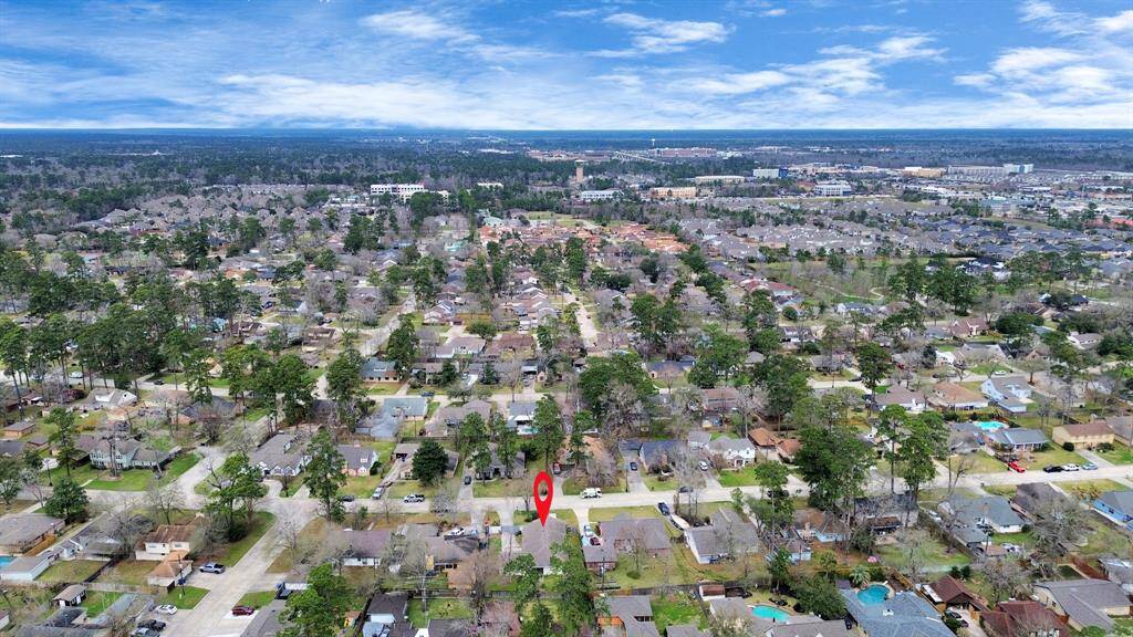 This aerial photo showcases a suburban neighborhood with abundant greenery and a mix of single-family homes. The area appears peaceful and spacious, with a red marker highlighting a specific property. The surroundings include nearby amenities and other residential developments, offering a sense of community.