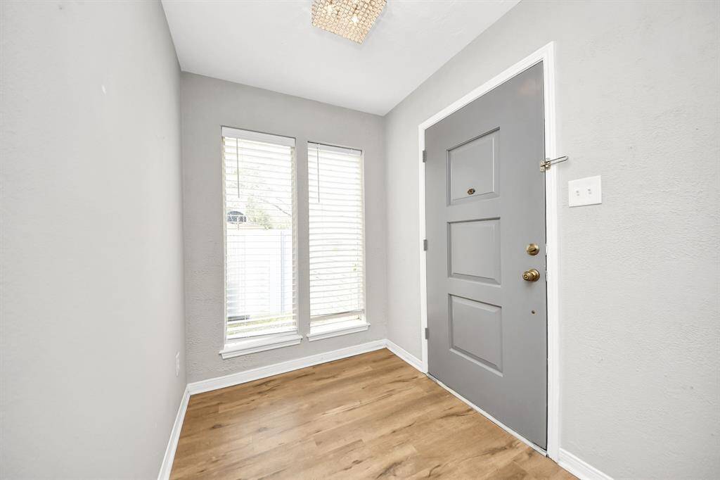 Bright entryway with a modern gray door, large windows for natural light, and warm wood flooring, creating a welcoming atmosphere.