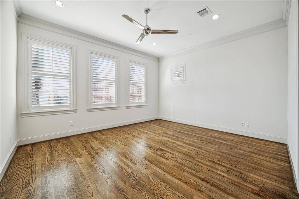 Another view of the primary suite with wood floors, large windows, crown molding...