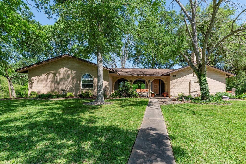 Welcoming ranch-style set on a lush, tree-shaded lot with great curb appeal. Features a charming covered front porch with arched openings, mature landscaping, and a wide walkway leading to the front door.