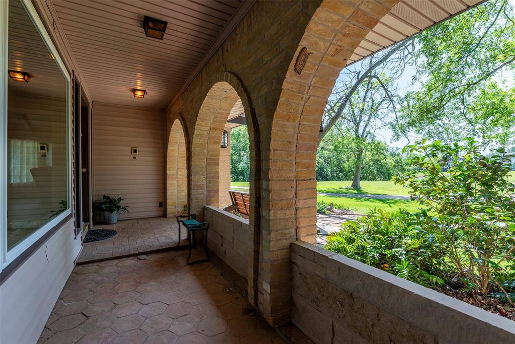 A covered front porch with classic brick arches and tile flooring offering a shaded peaceful space to enjoy the surrounding greenery.