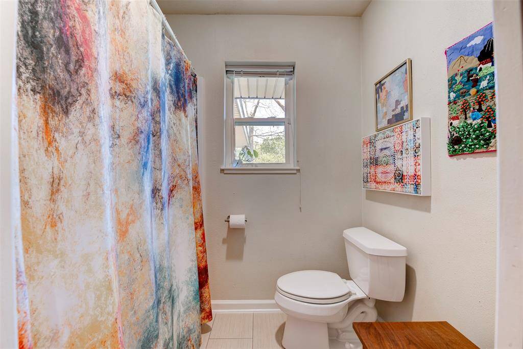 A full tub and shower combo sits behind a bold colorful shower curtain.  Bright natural light filters through the window.
