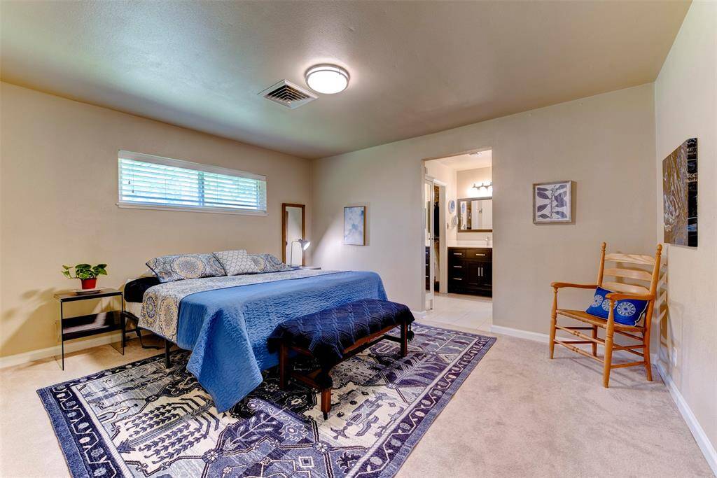Spacious and serene, the primary bedroom features plush carpeting, neutral walls, and ample light through a wide horizontal window. There's generous room for a kin-size bed and additional furniture while an en suite bath adds connivence and privacy.