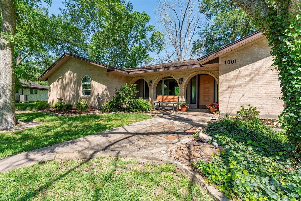 This captures a close-up view of the home's inviting exterior, showcasing mature shade trees while river rock stone complement the surrounding garden beds, blending seamlessly into the home's peaceful, shaded setting.