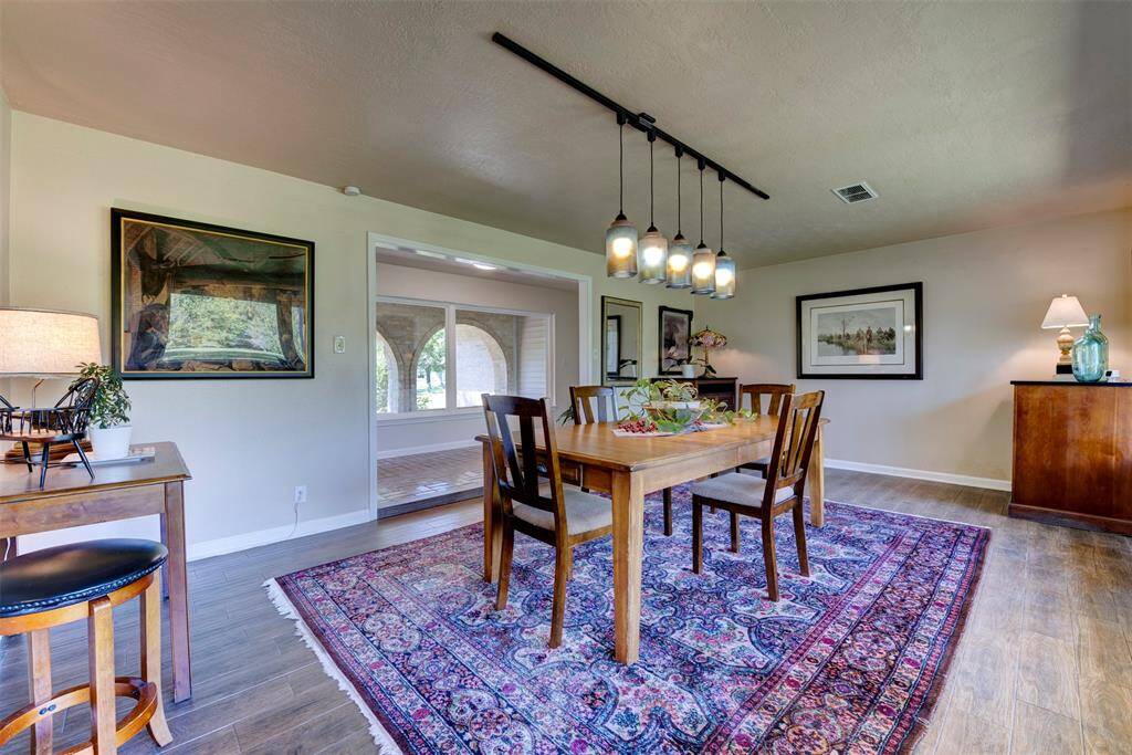 Spacious dining area featuring bold linear pendant lighting. A wide entryway frames the views of arched stone windows from the front patio, bringing in warm natural light and architectural interest.
